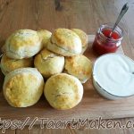 Luchtige zelfgemaakte scones met clotted cream en aardbeienjam op houten plank